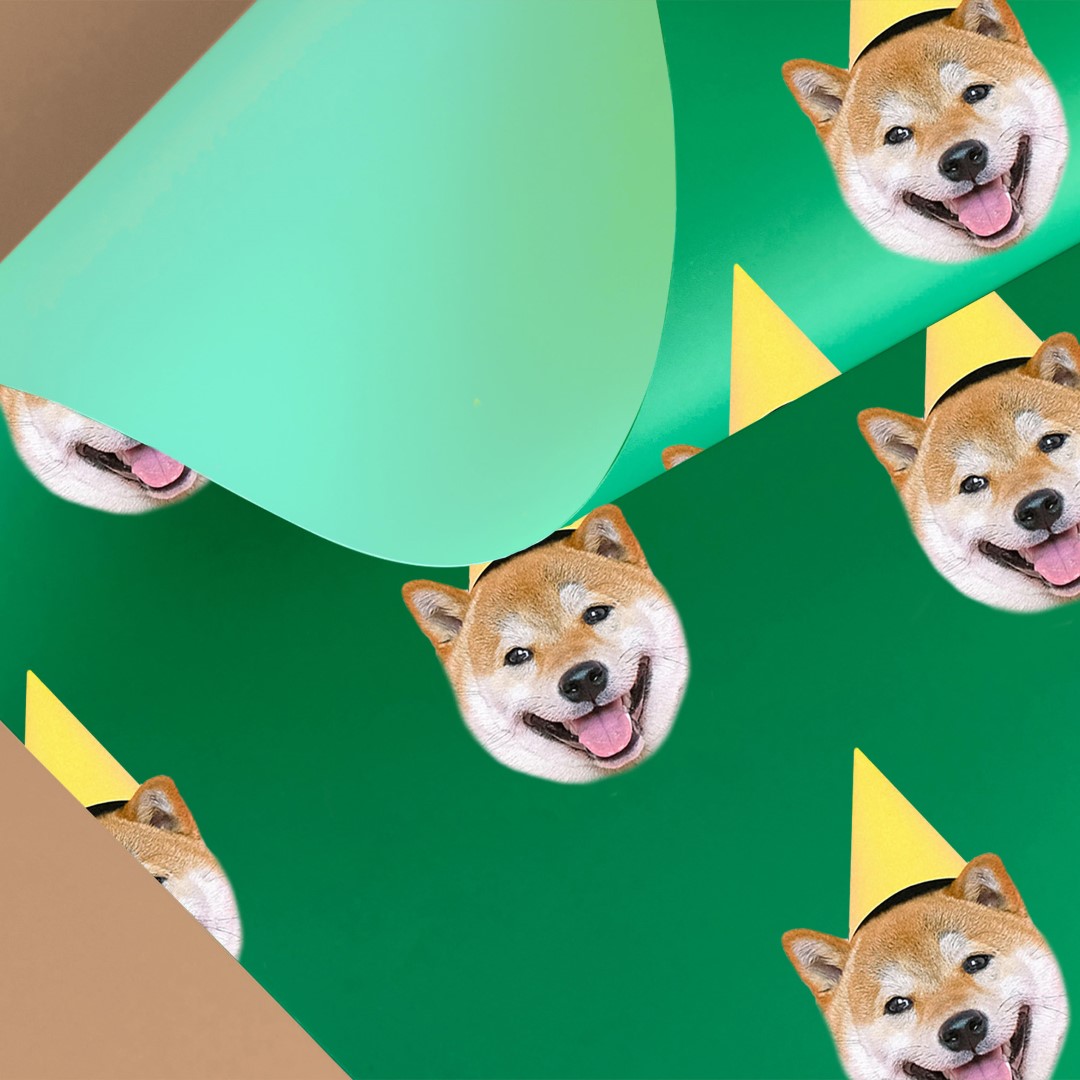 Custom gift wrap featuring a happy dog's face wearing a yellow party hat, printed on a green background and partially rolled up.